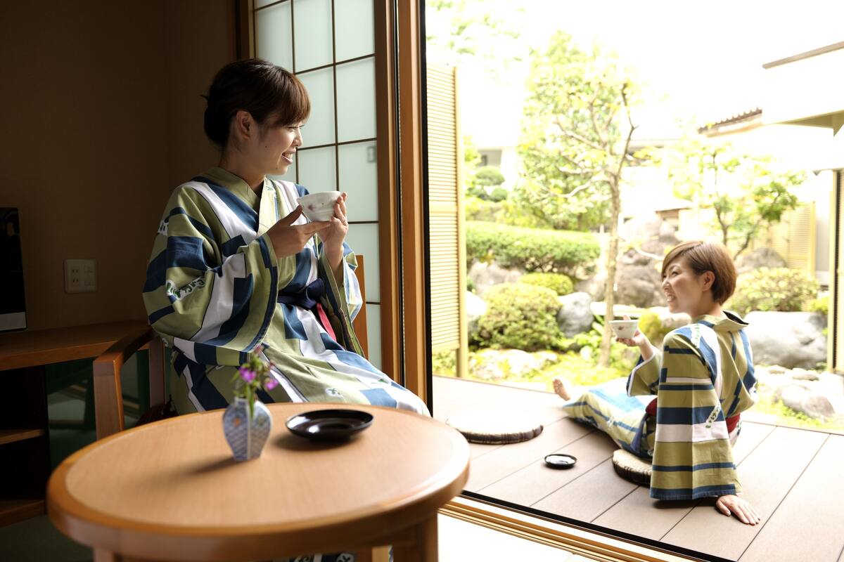 A traditional Japanese room with tatami flooring, a low table with a tea set, and a view of a garden through a sliding door.