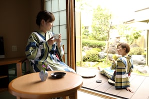 A traditional Japanese room with tatami flooring, a low table with a tea set, and a view of a garden through a sliding door. - Oyado Ikegami (Uozu)