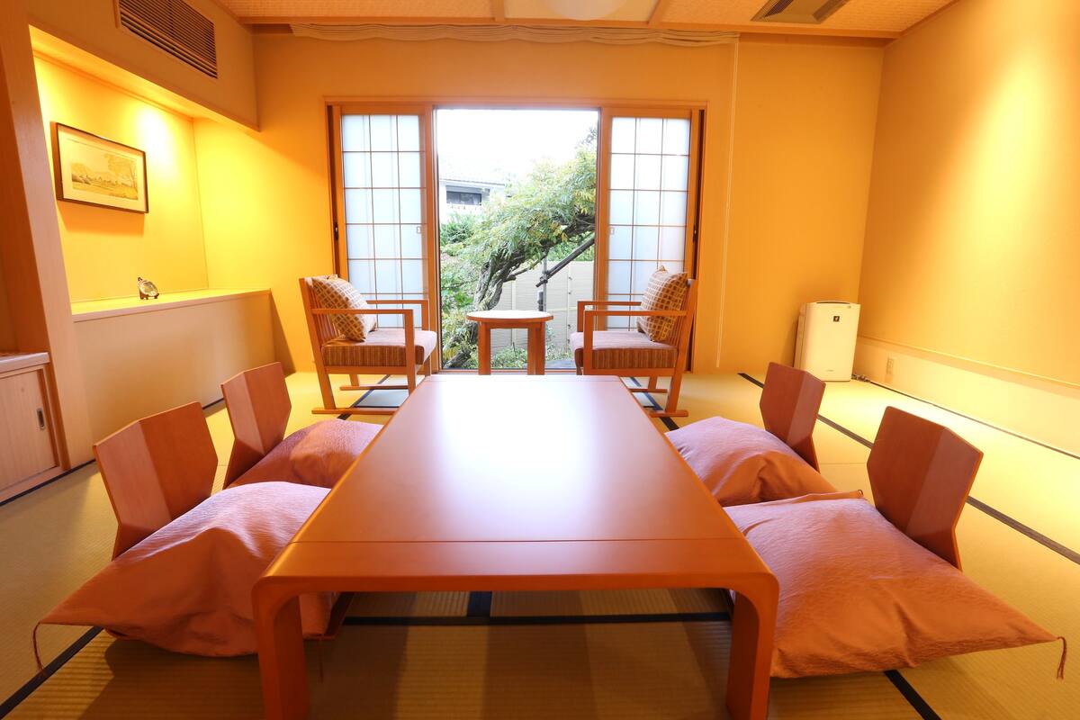 A room with tatami flooring, a low table, and four chairs.