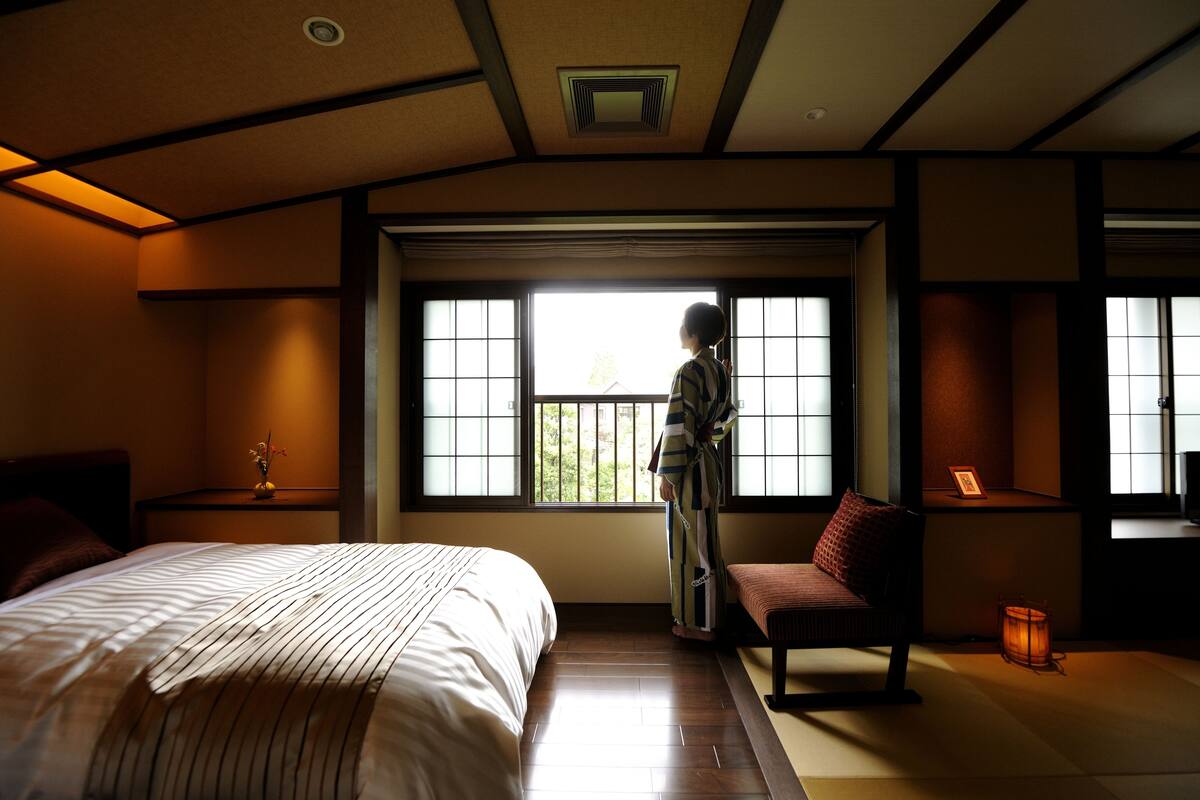 A traditional Japanese-style room with tatami flooring, a low wooden bed, a sliding door, and a small table with a vase.