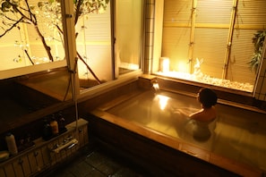 A traditional Japanese onsen with a wooden bathtub, a bamboo screen, and a small statue of a rabbit. - Oyado Ikegami (Uozu)