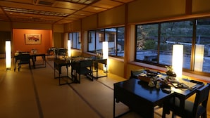 A traditional Japanese-style room with tatami flooring, low tables, and chairs. There are large windows providing views of the outside. - Oyado Ikegami (Uozu)