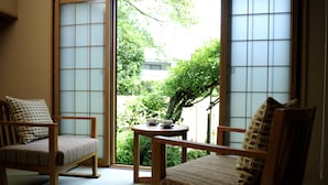 A traditional Japanese room with tatami flooring, two tatami mats, a low wooden table with a tea set, and sliding shoji doors leading to a garden. - Oyado Ikegami (Uozu)