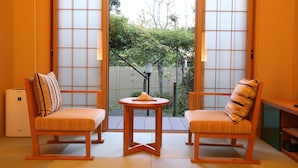 A traditional Japanese room with tatami flooring, two wooden chairs with cushions, a small round table, and a sliding door leading to an outdoor garden. - Oyado Ikegami (Uozu)