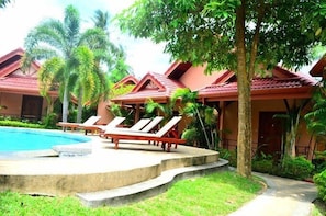 Un resort con piscina, sillones de descanso y exuberante vegetación tropical.