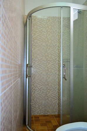 Un baño con cabina de ducha, paredes con azulejos y un inodoro.