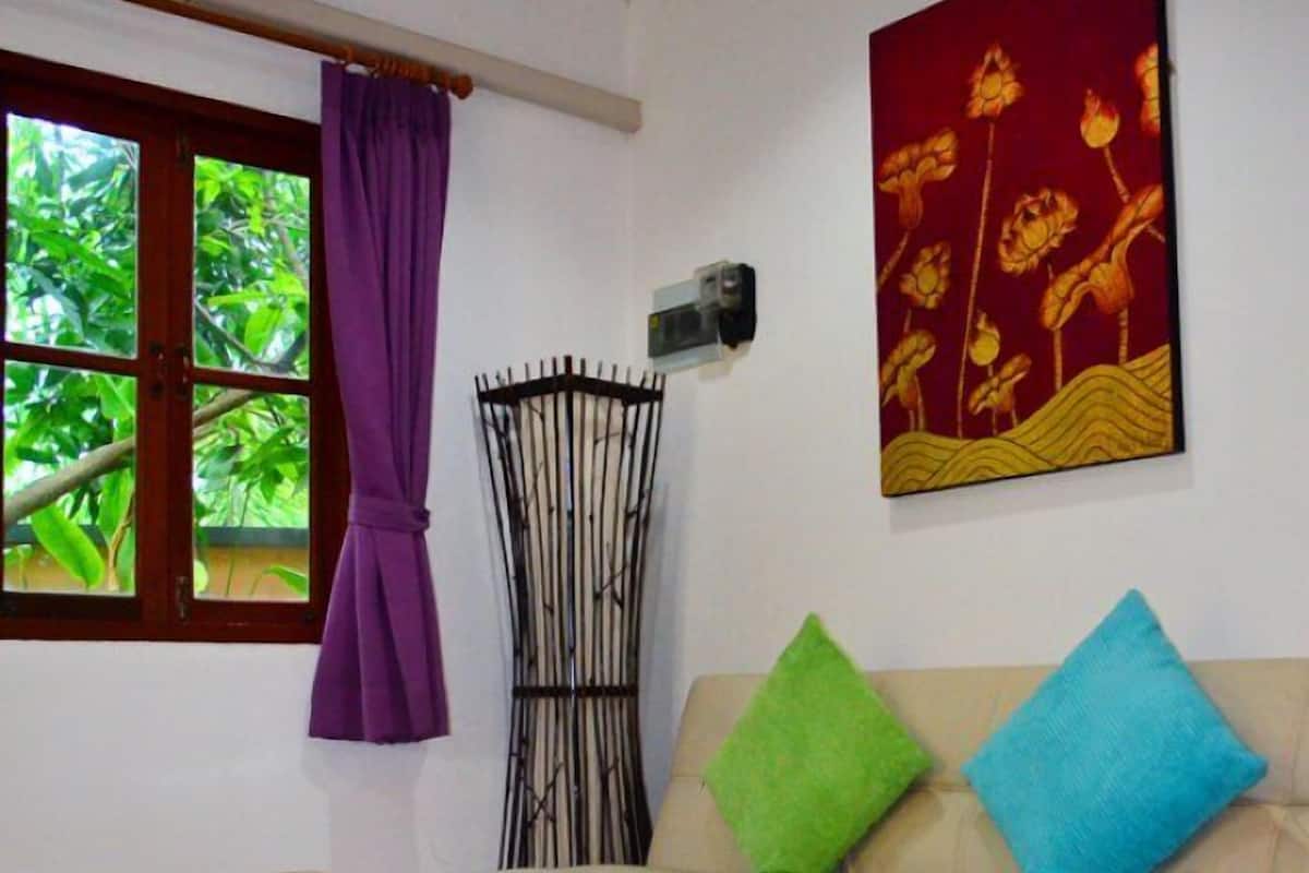 A living room with a sofa, a wooden coffee table, a patterned rug, a window with curtains, and a wall-mounted air conditioner.