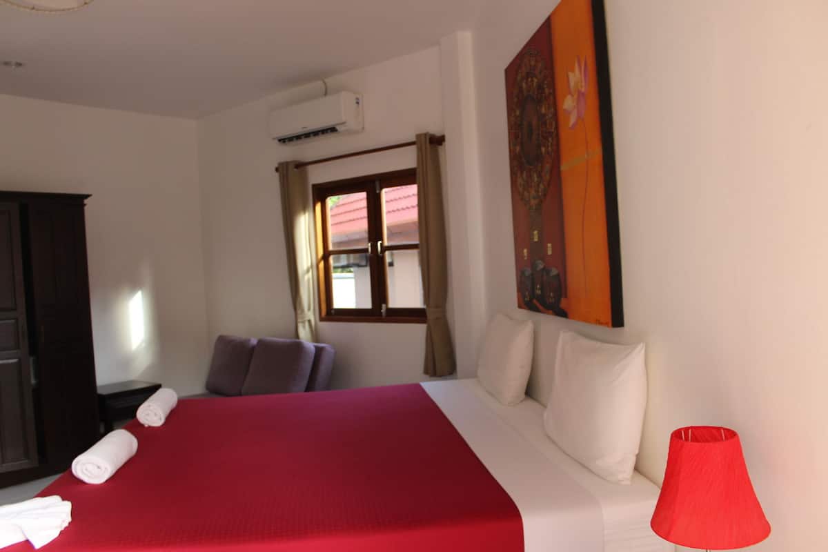 A hotel room with a large bed, a red lamp, a painting on the wall, and a window with curtains.