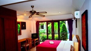 A hotel room with a bed, a desk, a television, and a balcony with a view of greenery. - The Happy Elephant Resort (Rawai)