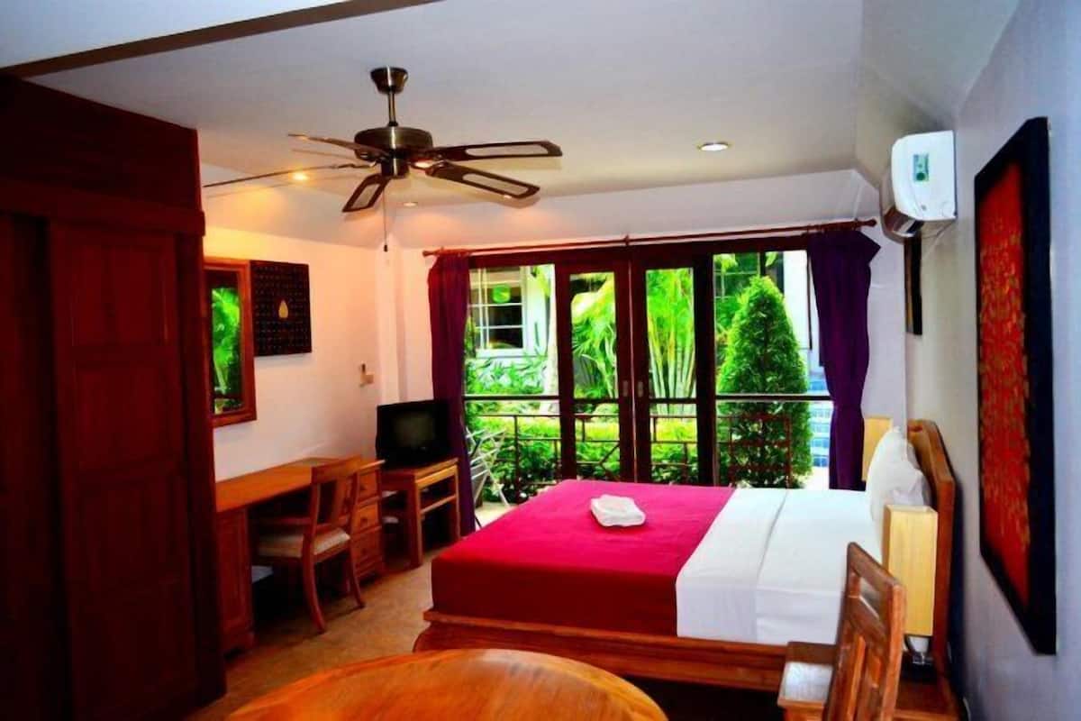 A hotel room with a bed, a desk, a television, and a balcony with a view of greenery.