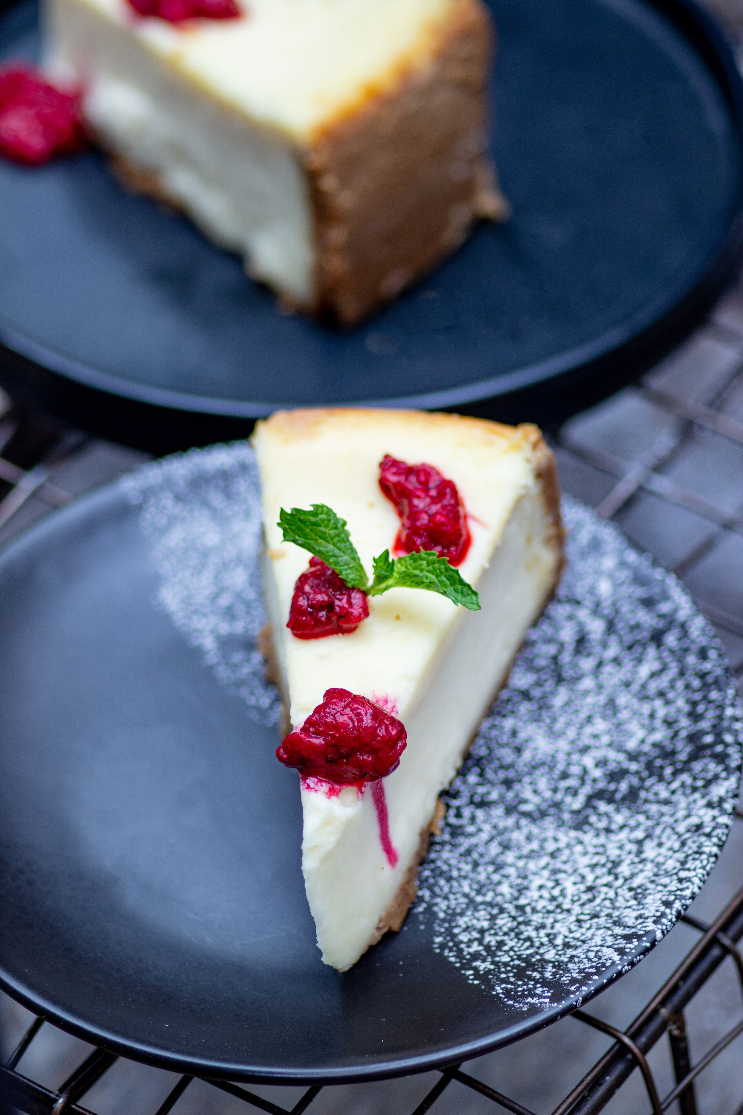 A slice of cheesecake on a plate with powdered sugar and raspberries.