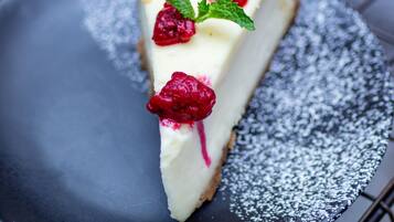A slice of cheesecake on a plate with powdered sugar and raspberries.