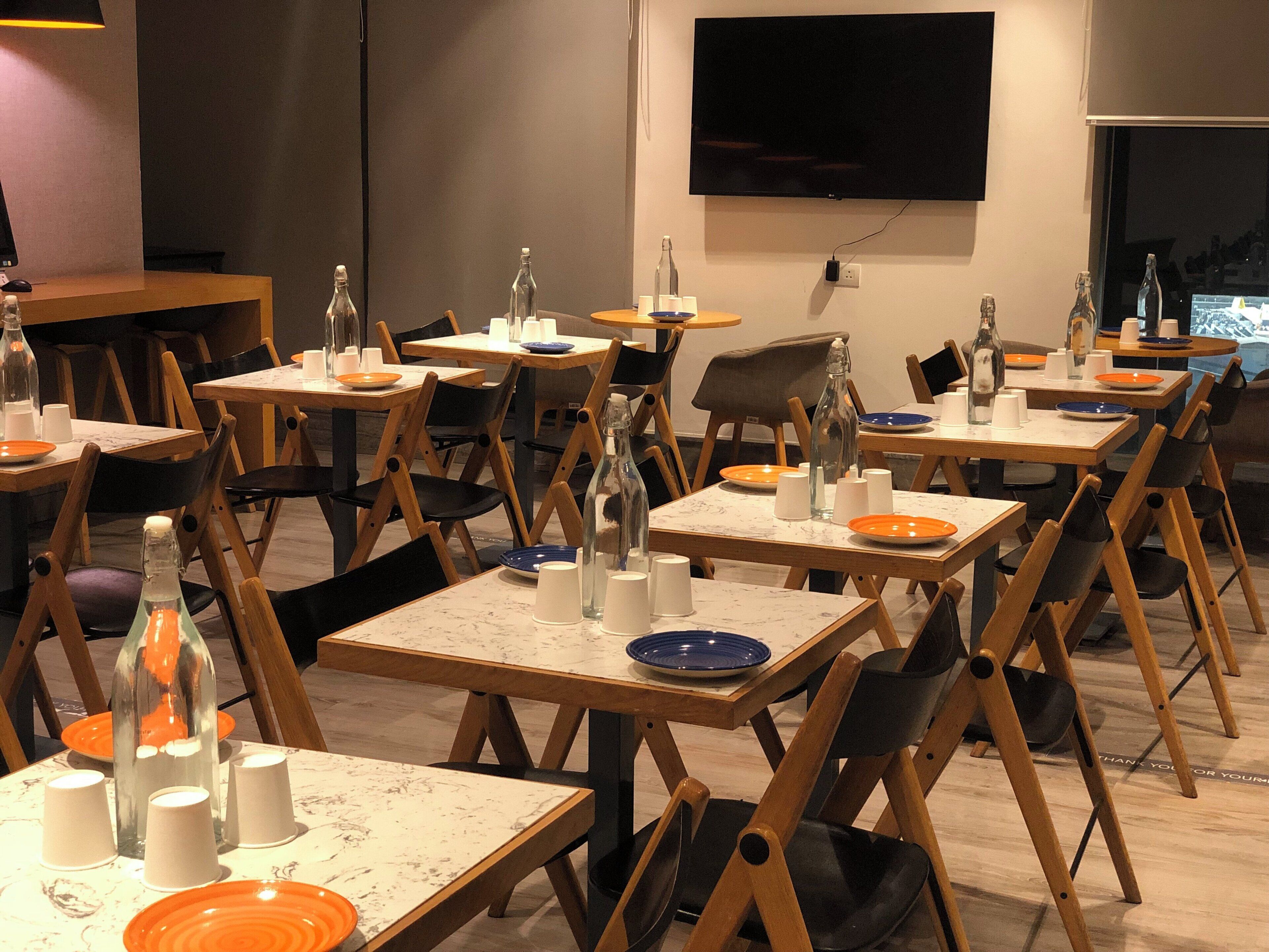 A dining area with multiple tables, chairs, and tables set with plates, cups, and bottles.