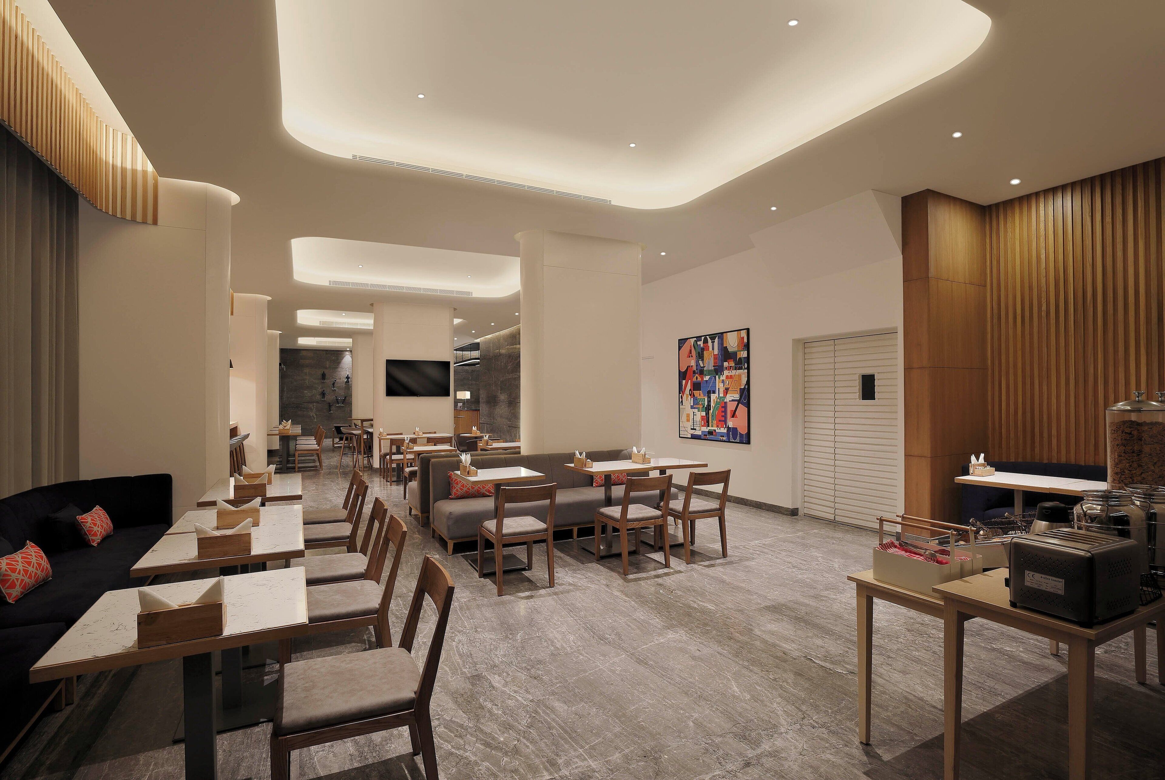 Un restaurant moderne avec un intérieur élégant, offrant différents types de sièges, notamment des tables et des banquettes, ainsi qu’un bar central.