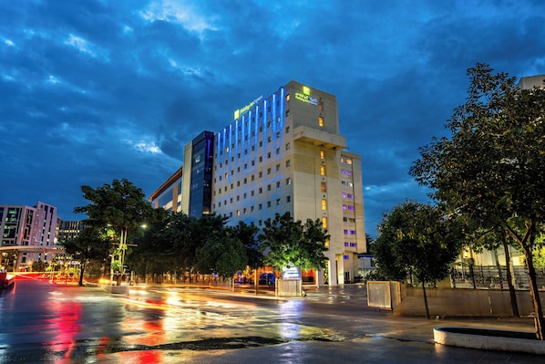 A hotel with multiple floors, a prominent sign at the top, and a parking lot with trees. - Holiday Inn Express Hyderabad Hitec City by IHG (Hyderabad)