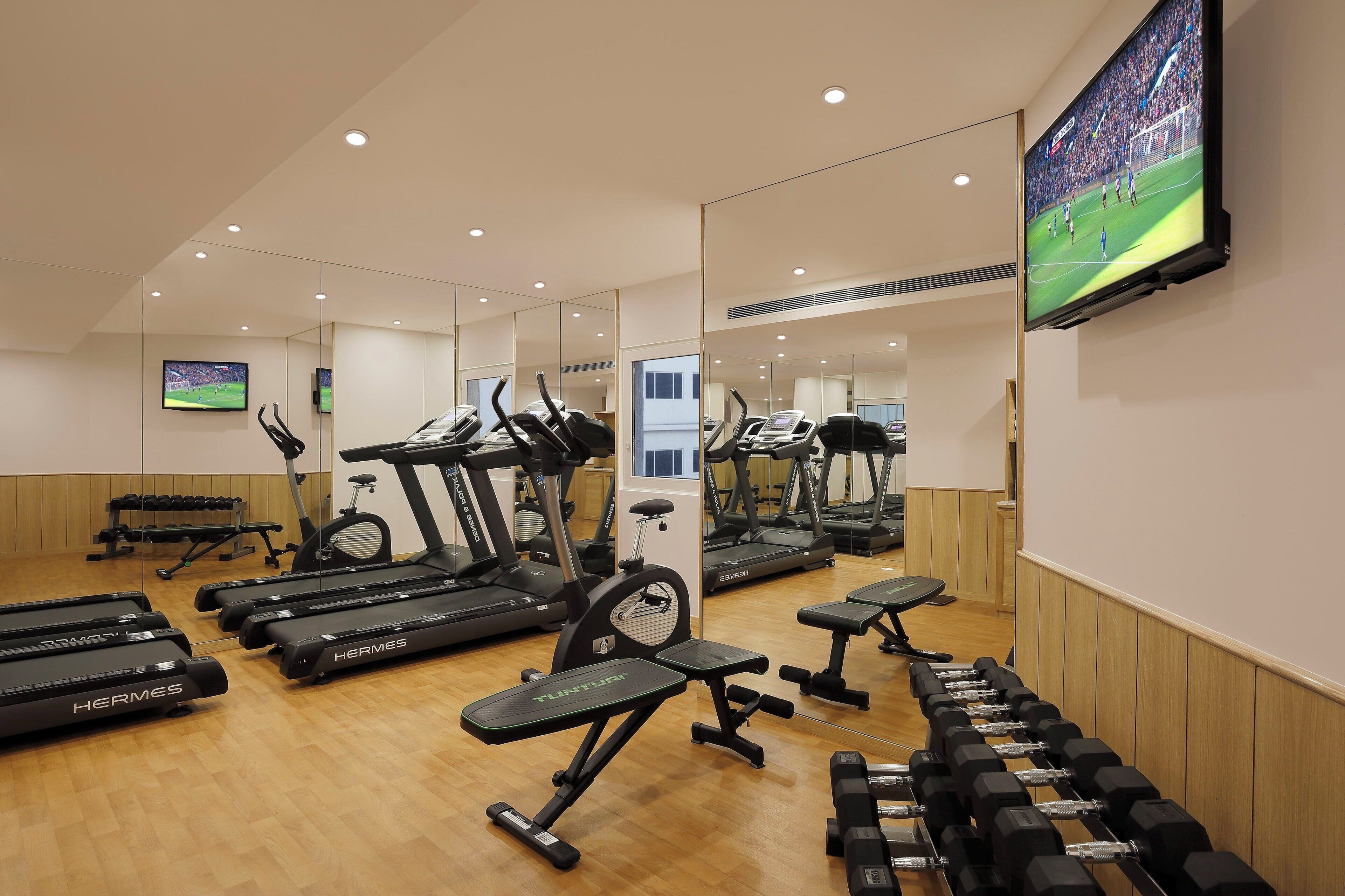 Et fitnesscenter med flere træningsmaskiner, herunder løbebånd og crosstrainere, samt vægte.