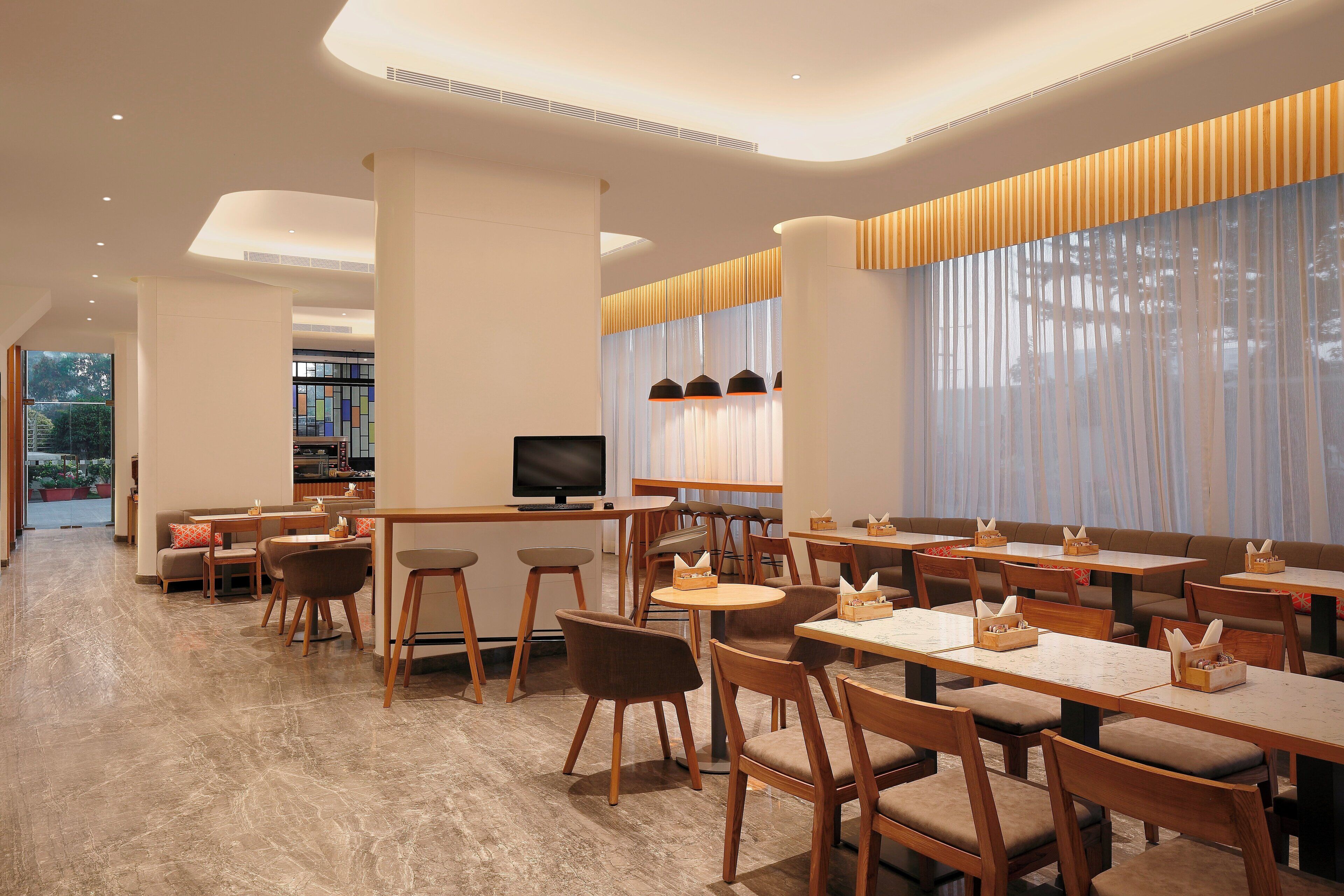 Un interior de restaurante moderno con varias zonas de estar, incluyendo mesas y cabinas, y un área de bar con una televisión.