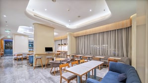 Un hall d’hôtel moderne, aménagé avec différents espaces de détente, notamment des canapés et des tables, ainsi qu’un grand écran de télévision.