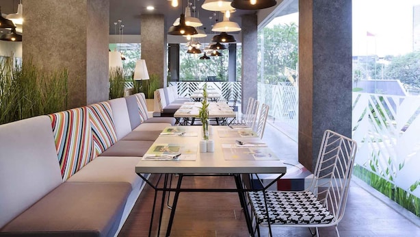 A modern restaurant with a long communal table, cushioned seating, and pendant lighting. - Ibis Styles Jakarta Sunter (Jakarta)
