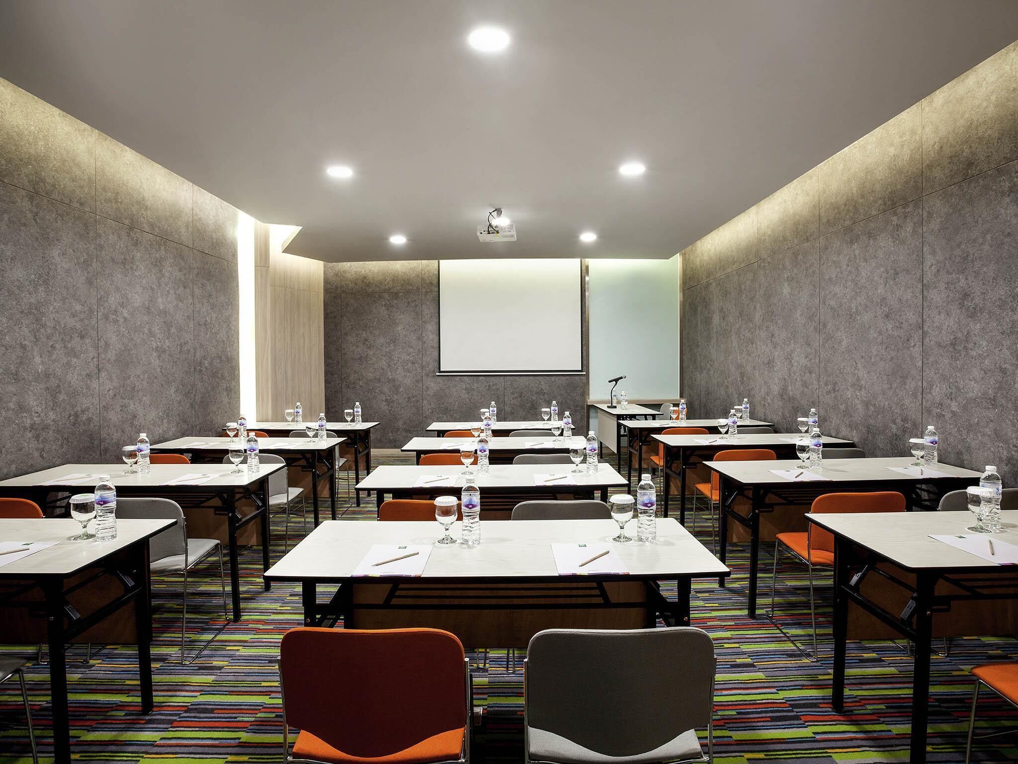 A conference room with multiple tables, chairs, and a projector screen.