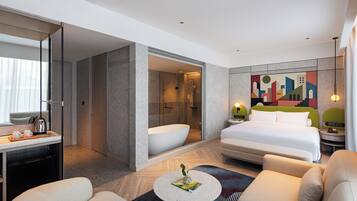 A modern hotel room with a bed, a sitting area, a bathroom, and a cityscape mural.