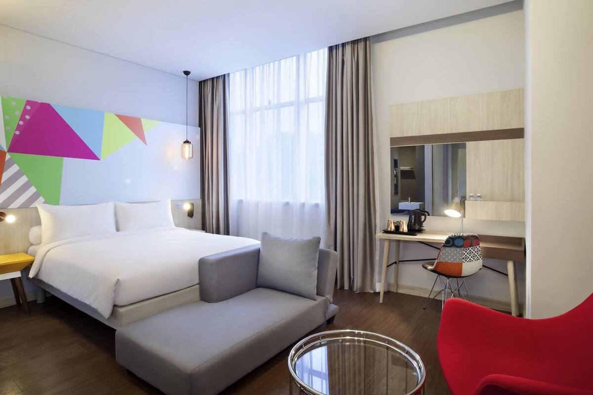 A hotel room with a bed, a sofa, a desk, a chair, and a round glass table.