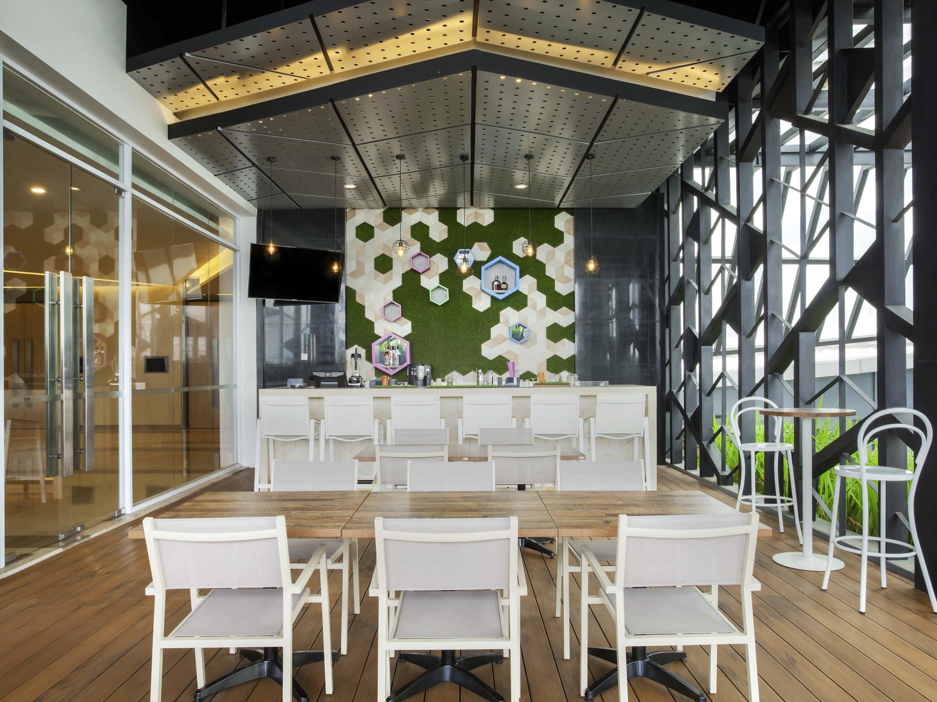Una sala de reuniones moderna con una larga mesa, sillas blancas, una zona de bar y una pared verde con patrones hexagonales.