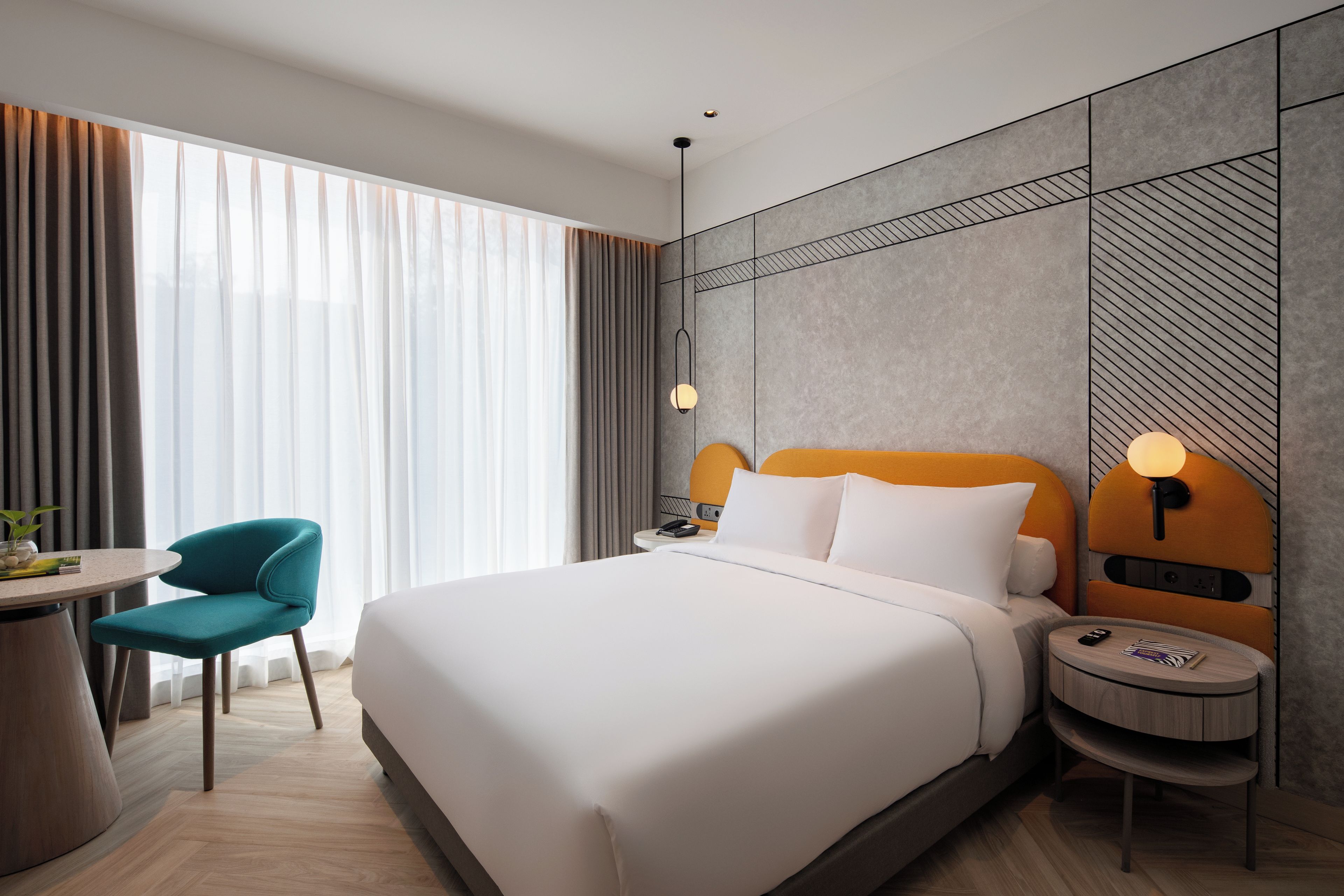 A hotel room with a bed, a desk, a chair, a nightstand, and a lamp.