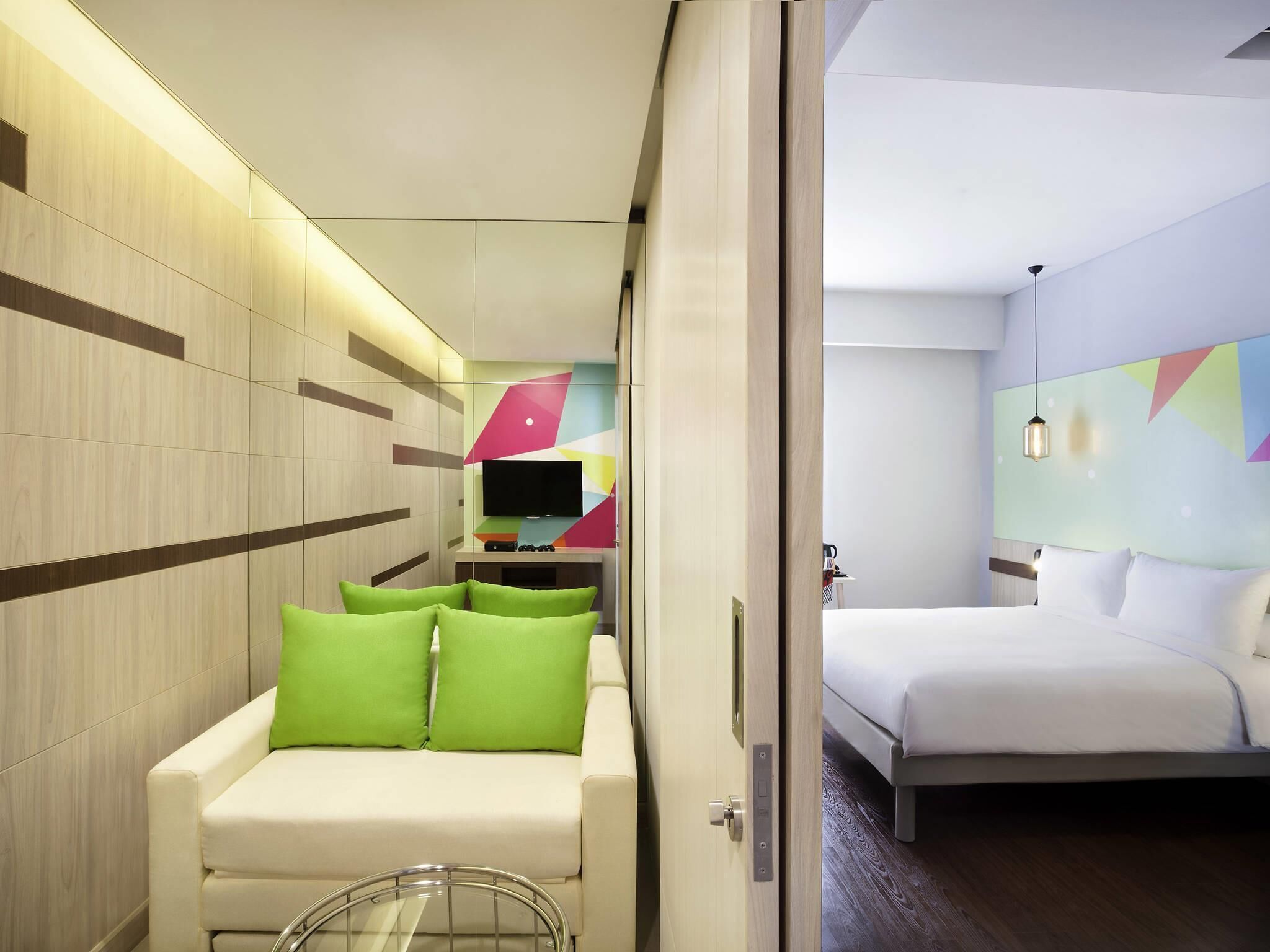 Una habitación de hotel moderna con sofá, cama, televisor y una pared con patrones geométricos.