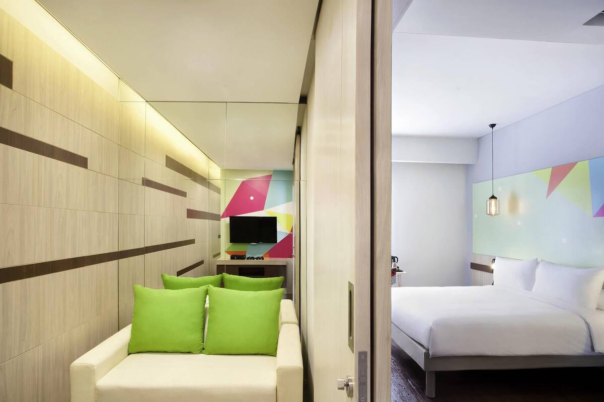 Una habitación de hotel moderna con sofá, cama, televisor y una pared con patrones geométricos.