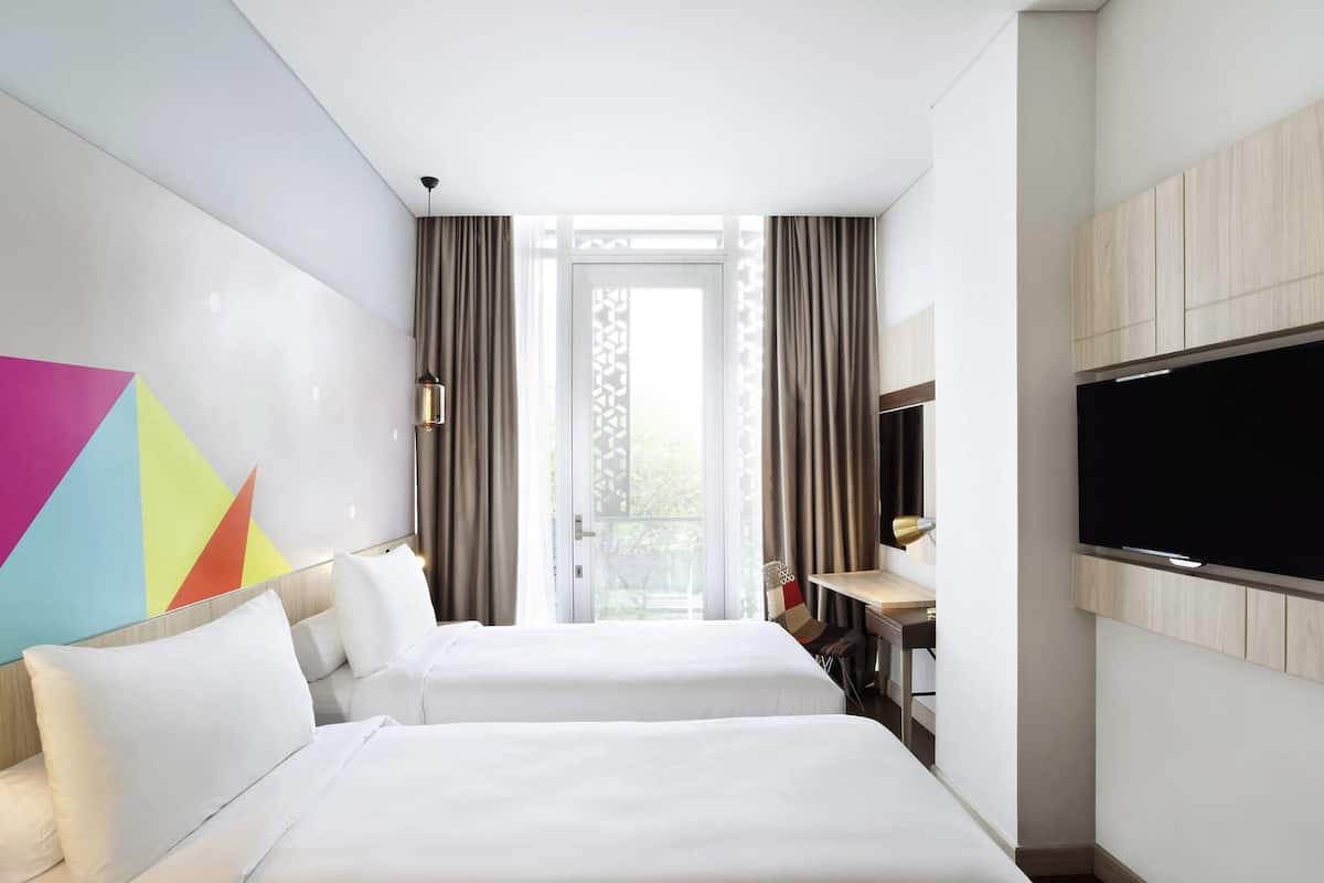 A hotel room with two beds, a TV, a desk, and a window with curtains.