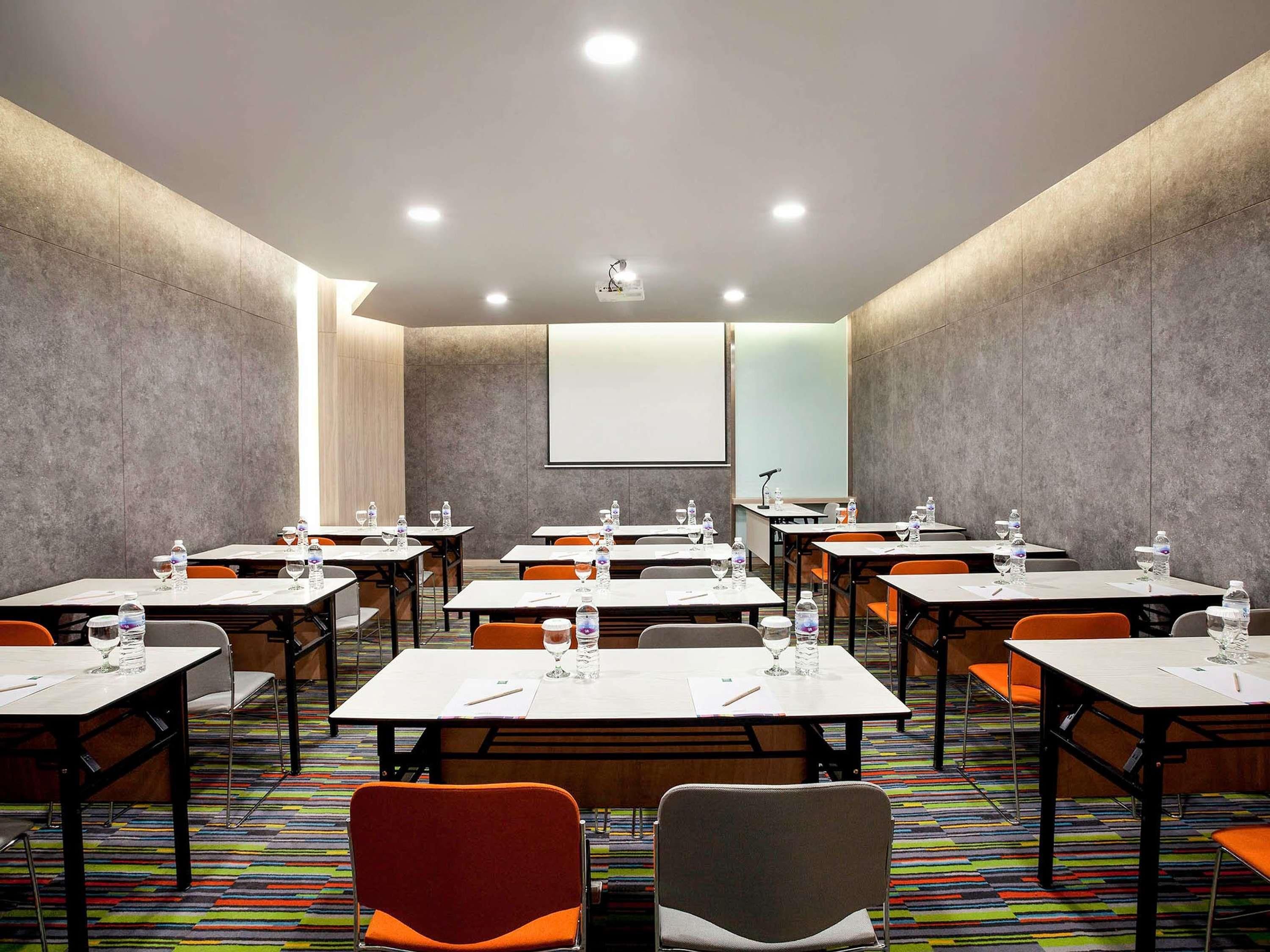 Un salón de conferencias con varias mesas, sillas y una pantalla para proyector.