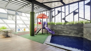 An indoor pool area with a slide, a table with chairs, and a view of the sky through large windows. - Ibis Styles Jakarta Sunter (Jakarta)