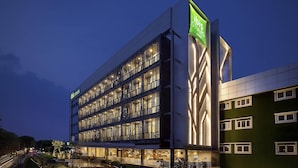 A multi-story hotel with a modern facade, illuminated windows, and a prominent green sign indicating the hotel's name. - Ibis Styles Jakarta Sunter (Jakarta)