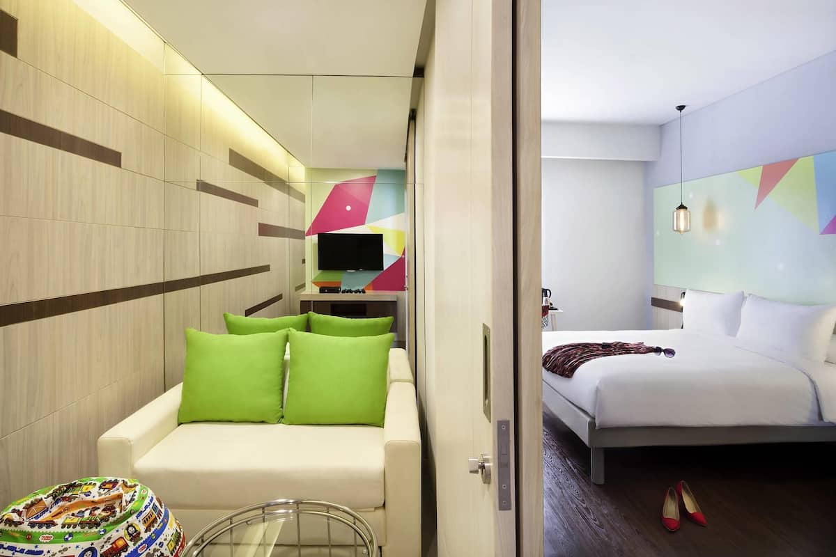 A modern hotel room with a sofa, a bed, a TV, and a colorful wall decoration.