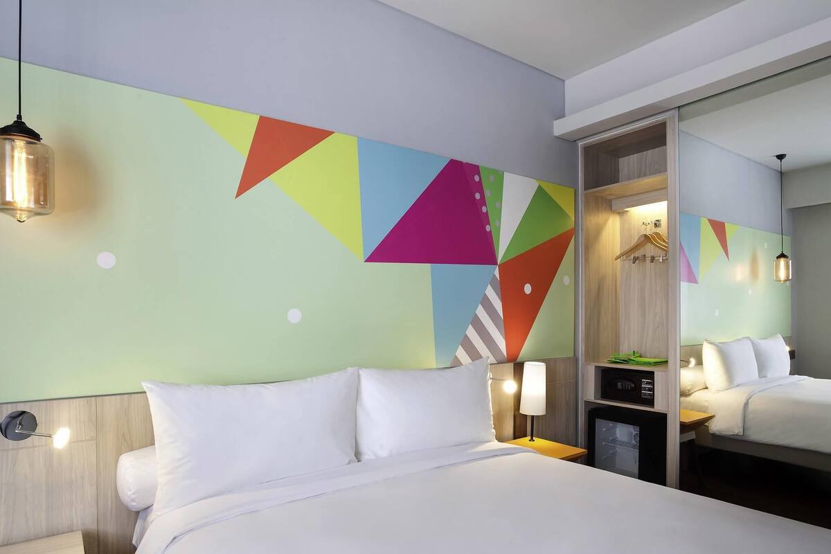 A hotel room with a bed, bedside table, lamp, and a mirror.