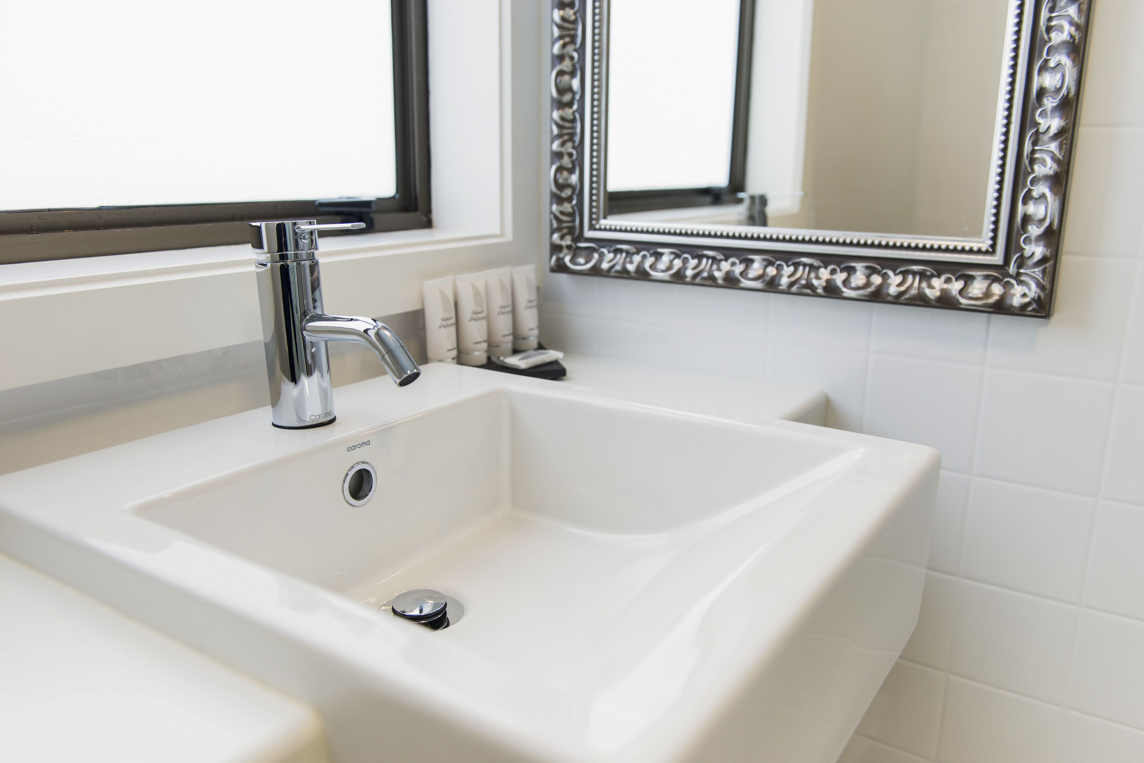 A bathroom with a white sink, chrome faucet, and a decorative mirror with an ornate frame.