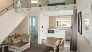 Una habitación de hotel moderna con una escalera de cristal, kitchenette, sofá y zona de comedor.