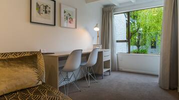 A hotel room with a bed, a desk with two chairs, a lamp, and a window with curtains.