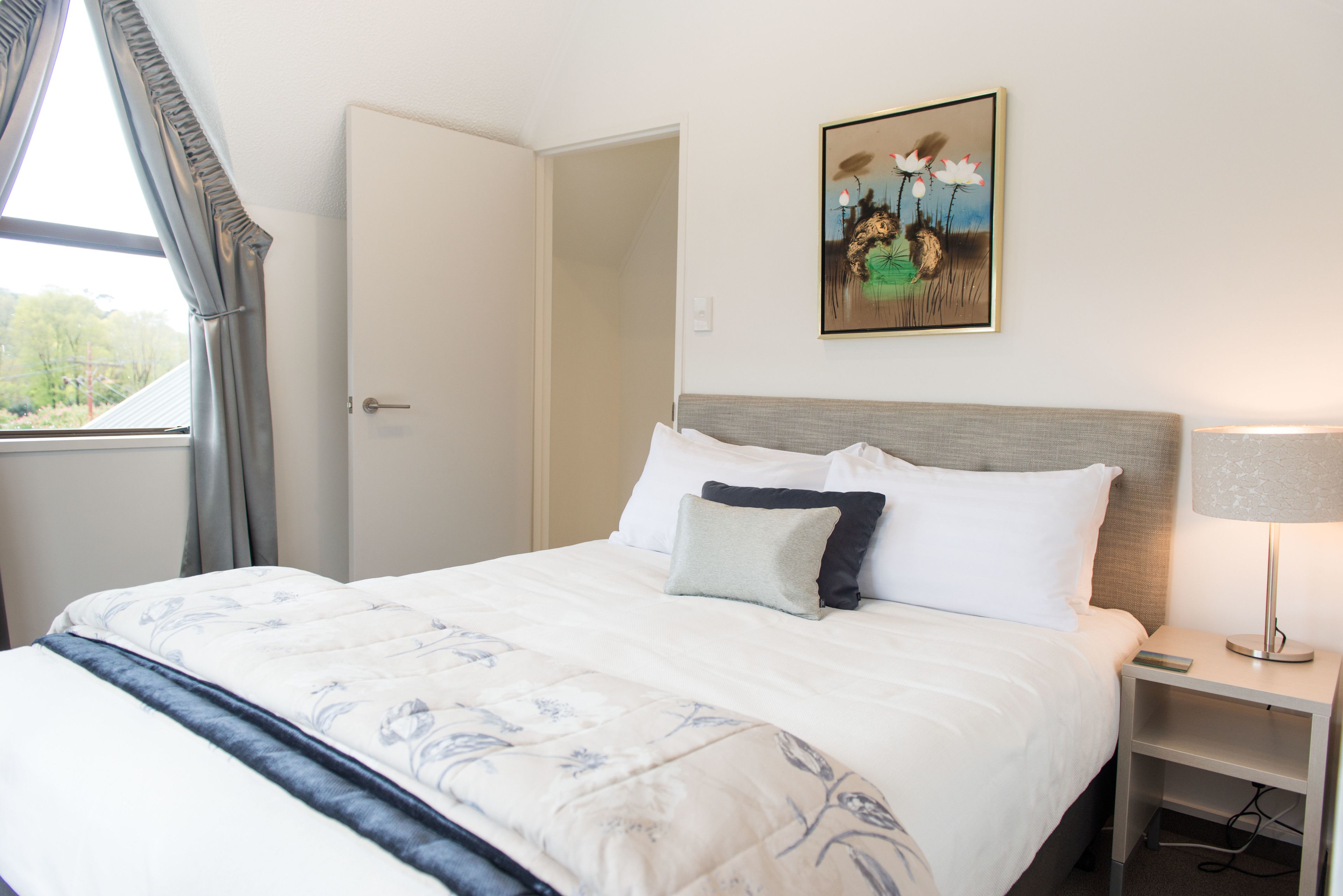 Una cama bien hecha con una colcha estampada con motivos florales, una lámpara de noche y un cuadro en la pared.