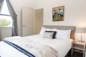 Una cama bien hecha con una colcha estampada con motivos florales, una lámpara de noche y un cuadro en la pared.