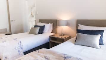 A hotel room with two beds, each with a nightstand, a lamp, and a door.