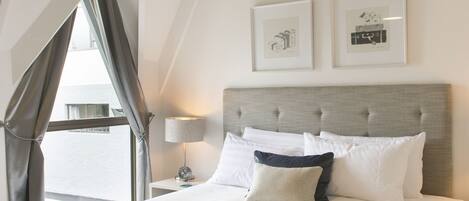 A modern hotel room with a large bed, a nightstand, a lamp, and framed artwork on the wall.