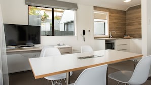 Una cocina moderna con comedor, que incluye un televisor, sillas blancas y una mesa de madera.