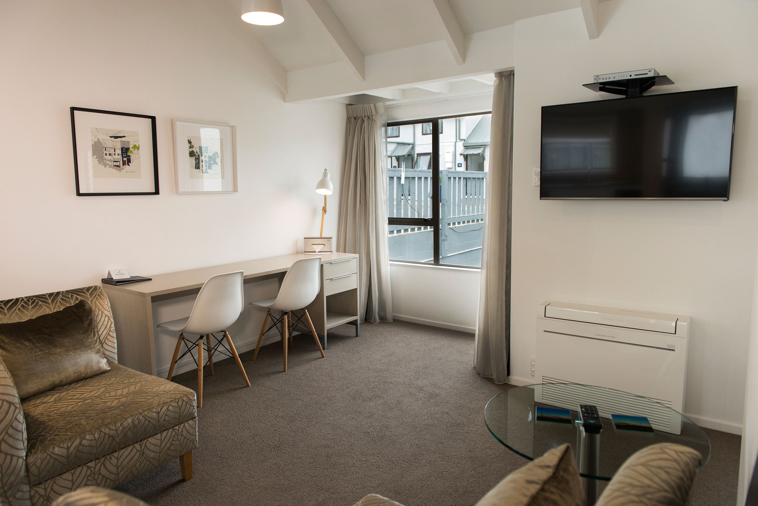Une chambre d’hôtel équipée d’un bureau, de deux chaises, d’un canapé, d’une télévision et d’une fenêtre donnant sur des immeubles.