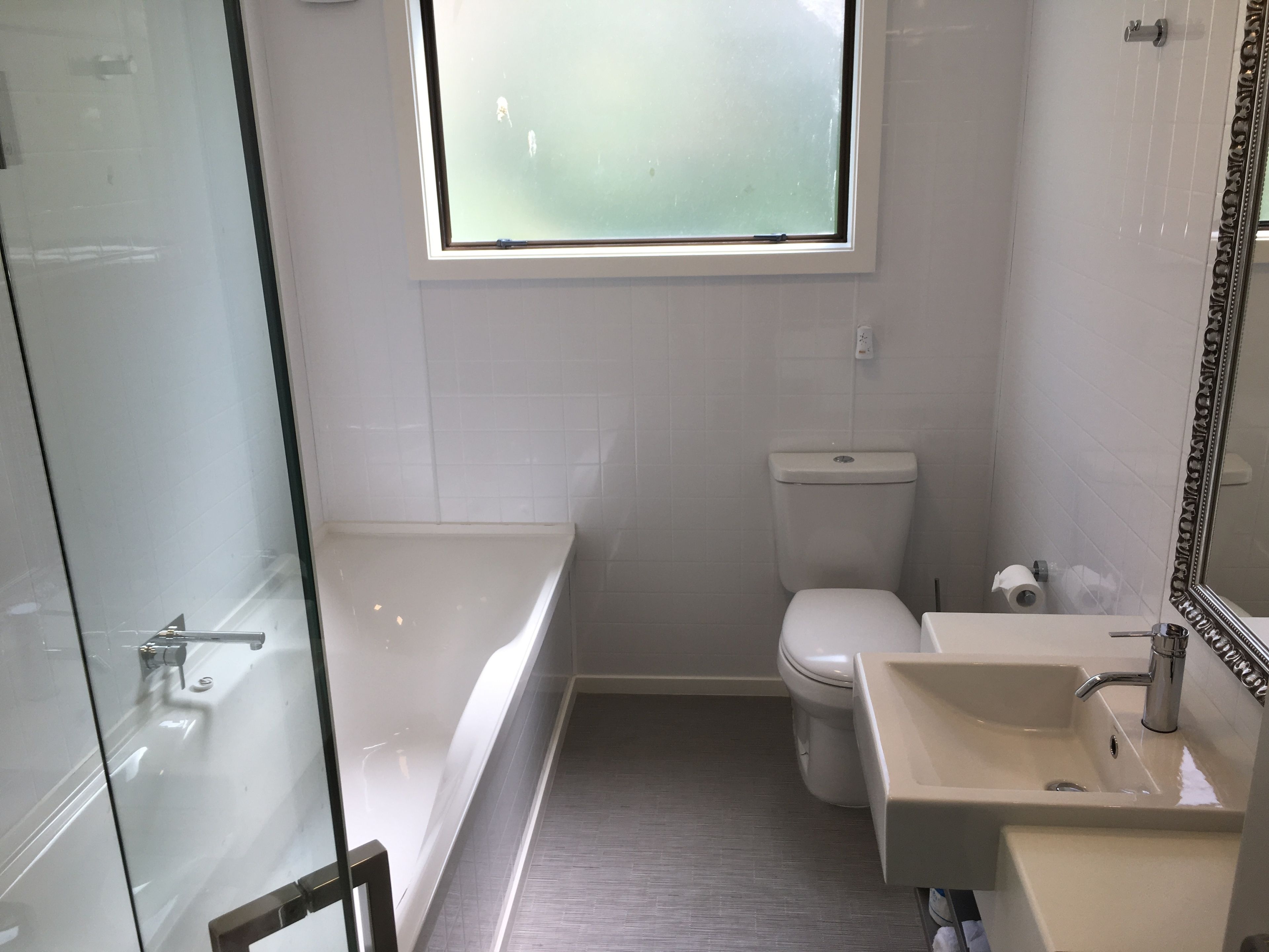 Un baño con cabina de ducha de vidrio, inodoro y lavamanos con espejo.