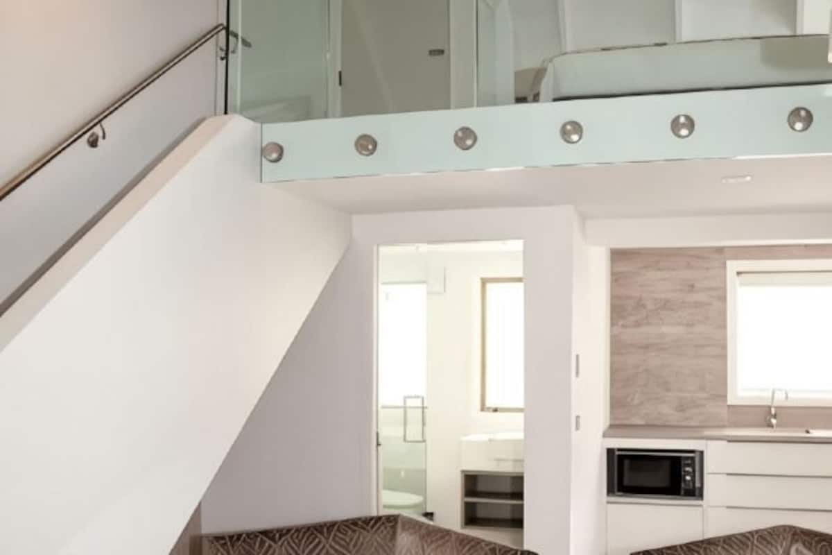 A modern kitchen with a microwave, a glass staircase, and a view into another room.