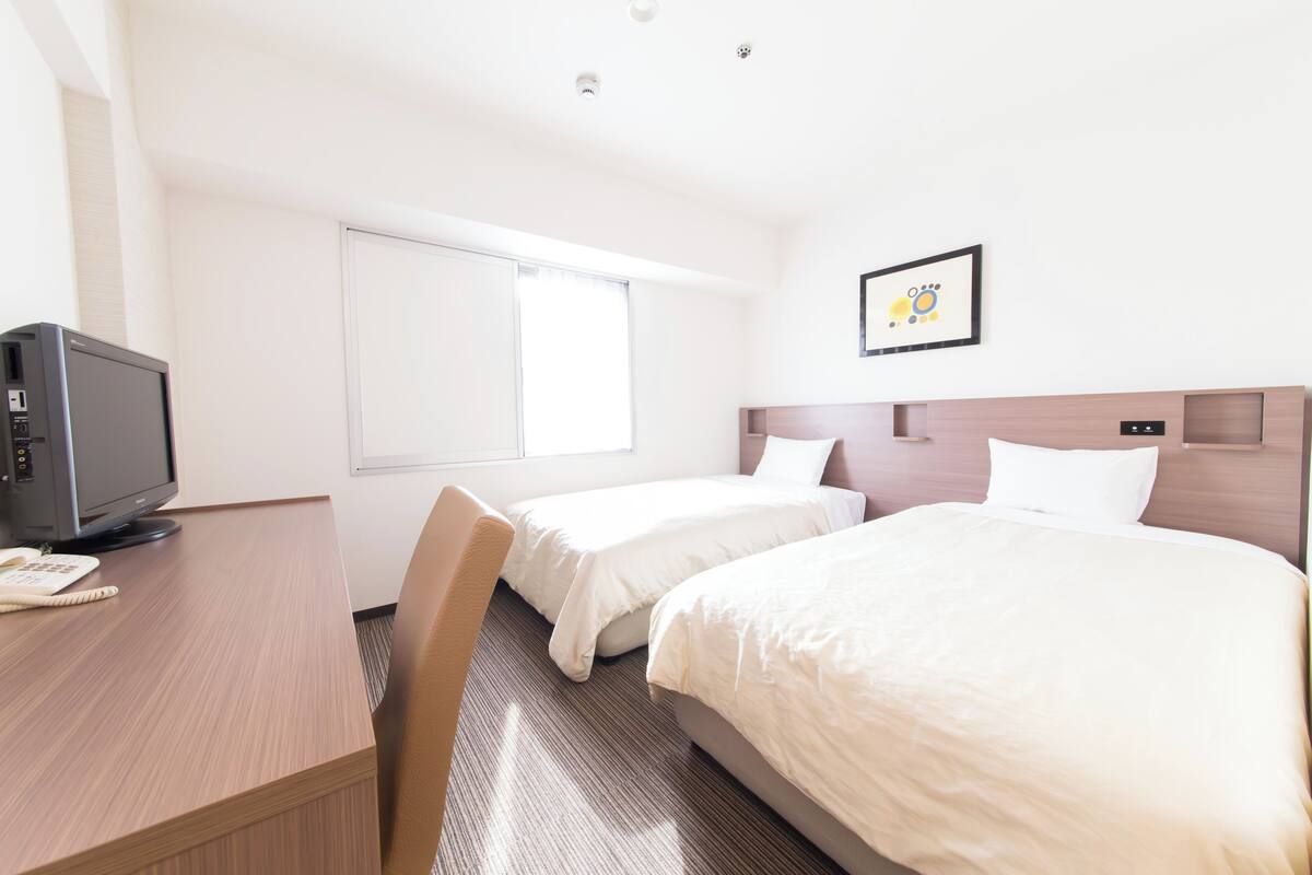 A hotel room with two beds, a desk with a computer, and a window.