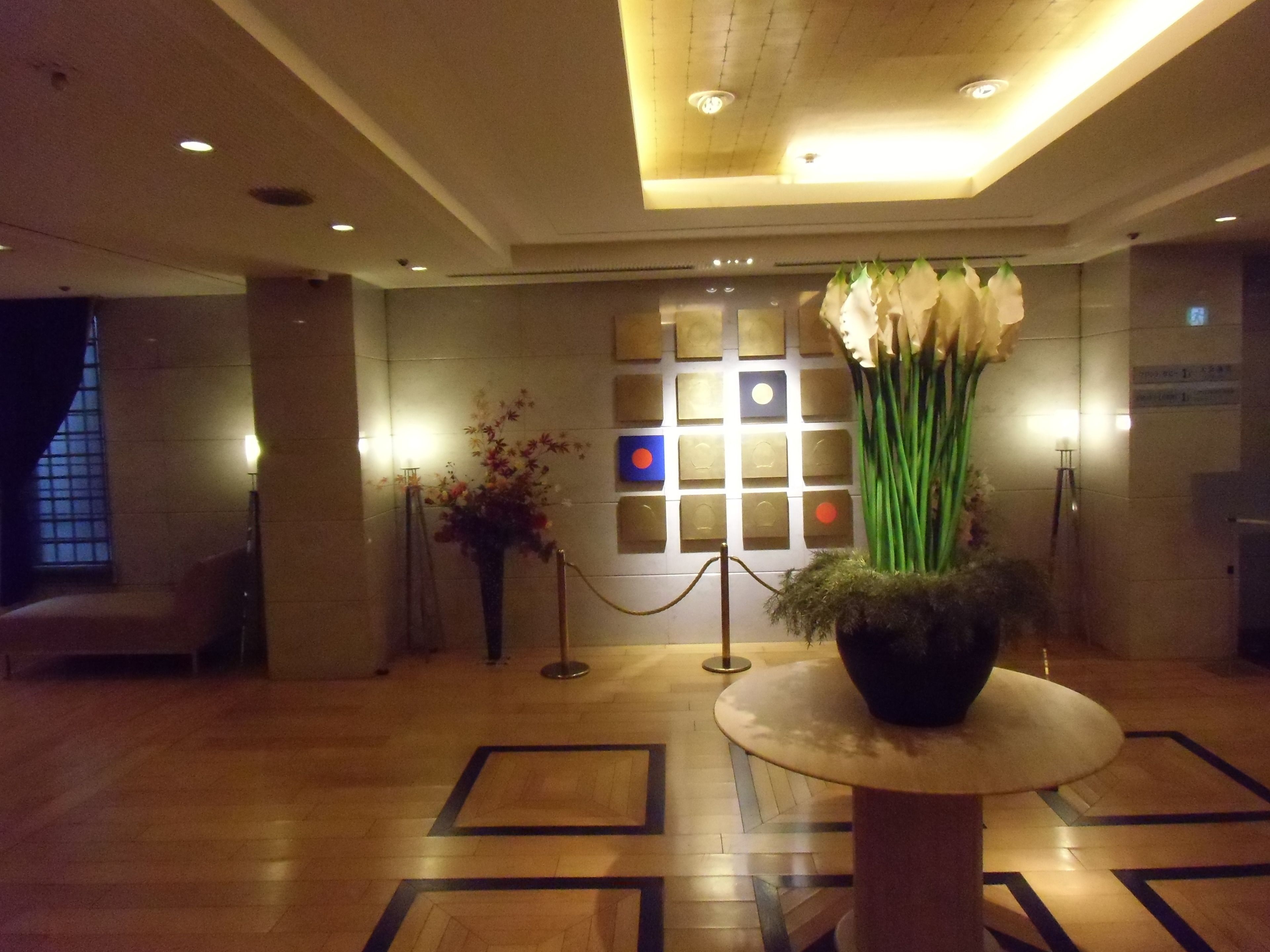 A lobby with a reception desk, a large vase of flowers, a seating area, and a patterned floor.