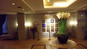 A lobby with a reception desk, a large vase of flowers, a seating area, and a patterned floor.